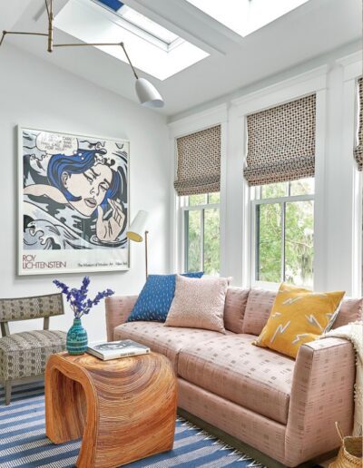 Sitting room in the 2018 Coastal Living Idea House with skylights, a blush sofa, a rattan table, and a blue striped rug.