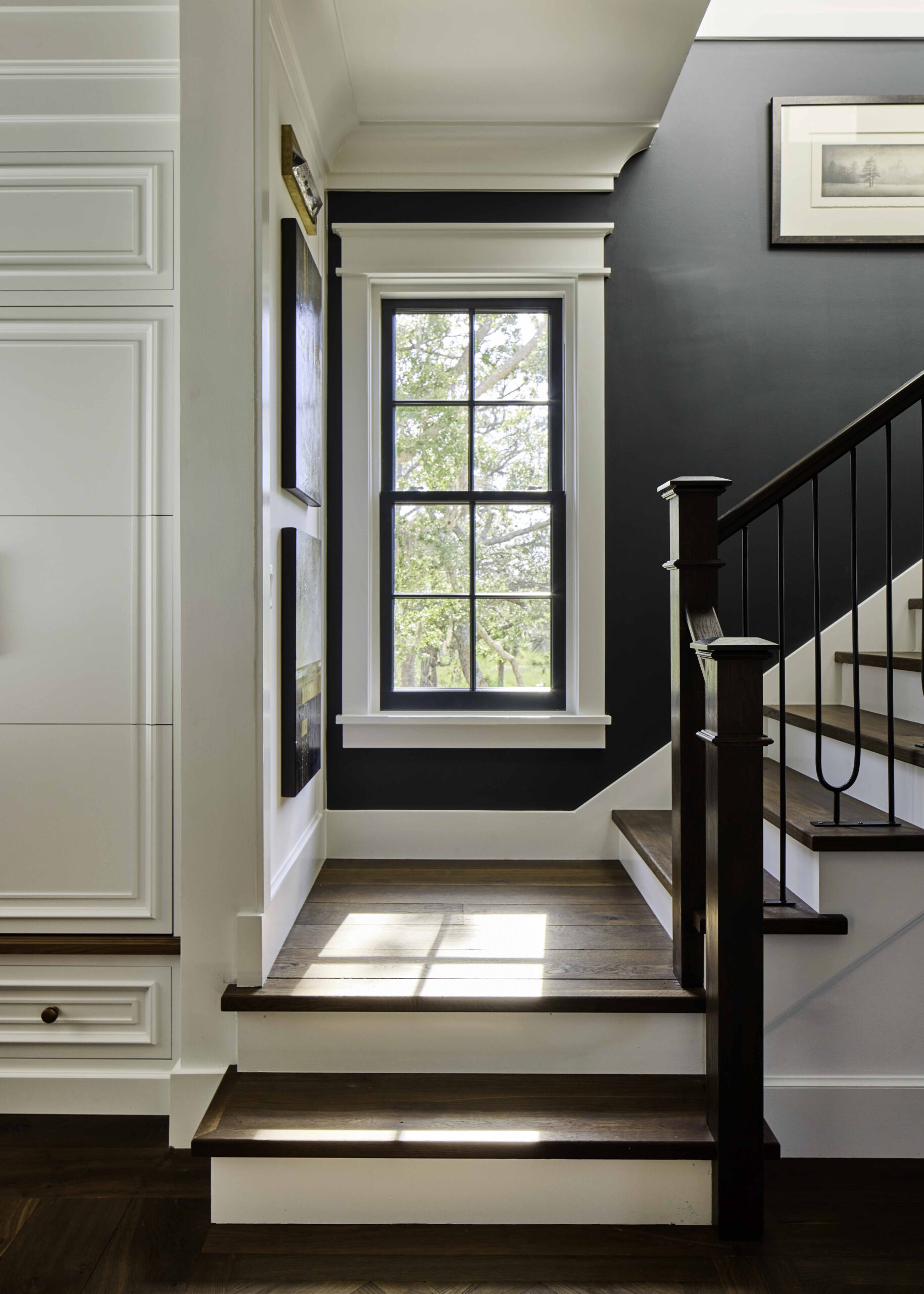 Staircase landing with dark hardwood treads, black metal railing, and a tall window in the 2025 Southern Living Showcase Home in Habersham, SC, built by Allen Patterson Builders