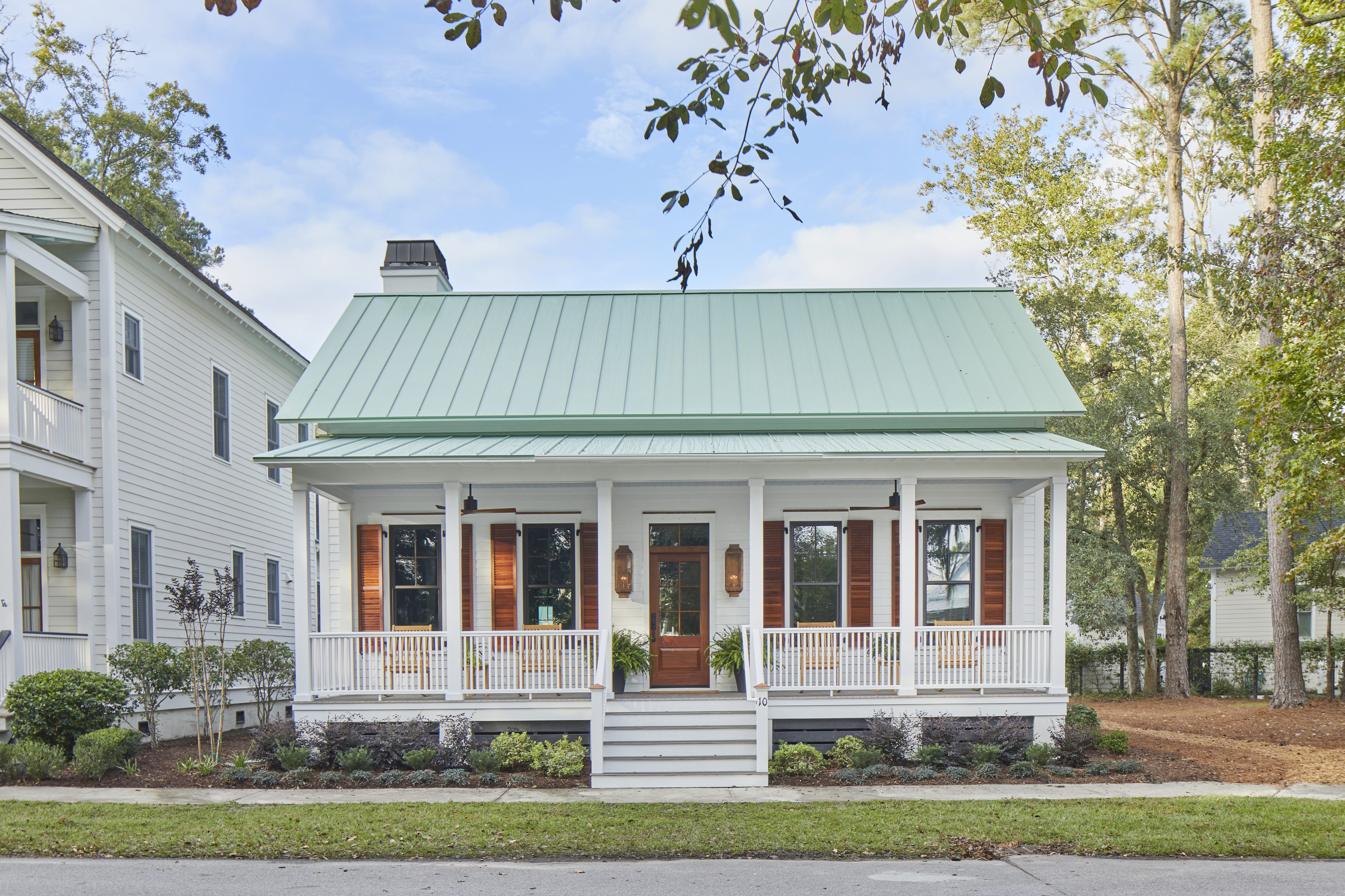 Front exterior of the 2020 Southern Living Showcase Home in Habersham, Beaufort, SC, a white raised cottage with a green standing-seam metal roof, full-width front porch, mahogany front door, and wood louvered shutters.