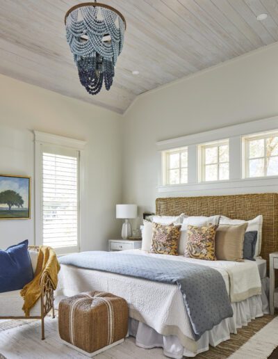 Primary bedroom with a woven rattan headboard, ombré blue beaded chandelier, and whitewashed shiplap ceiling in the 2020 Southern Living Showcase Home in Habersham, Beaufort, SC.