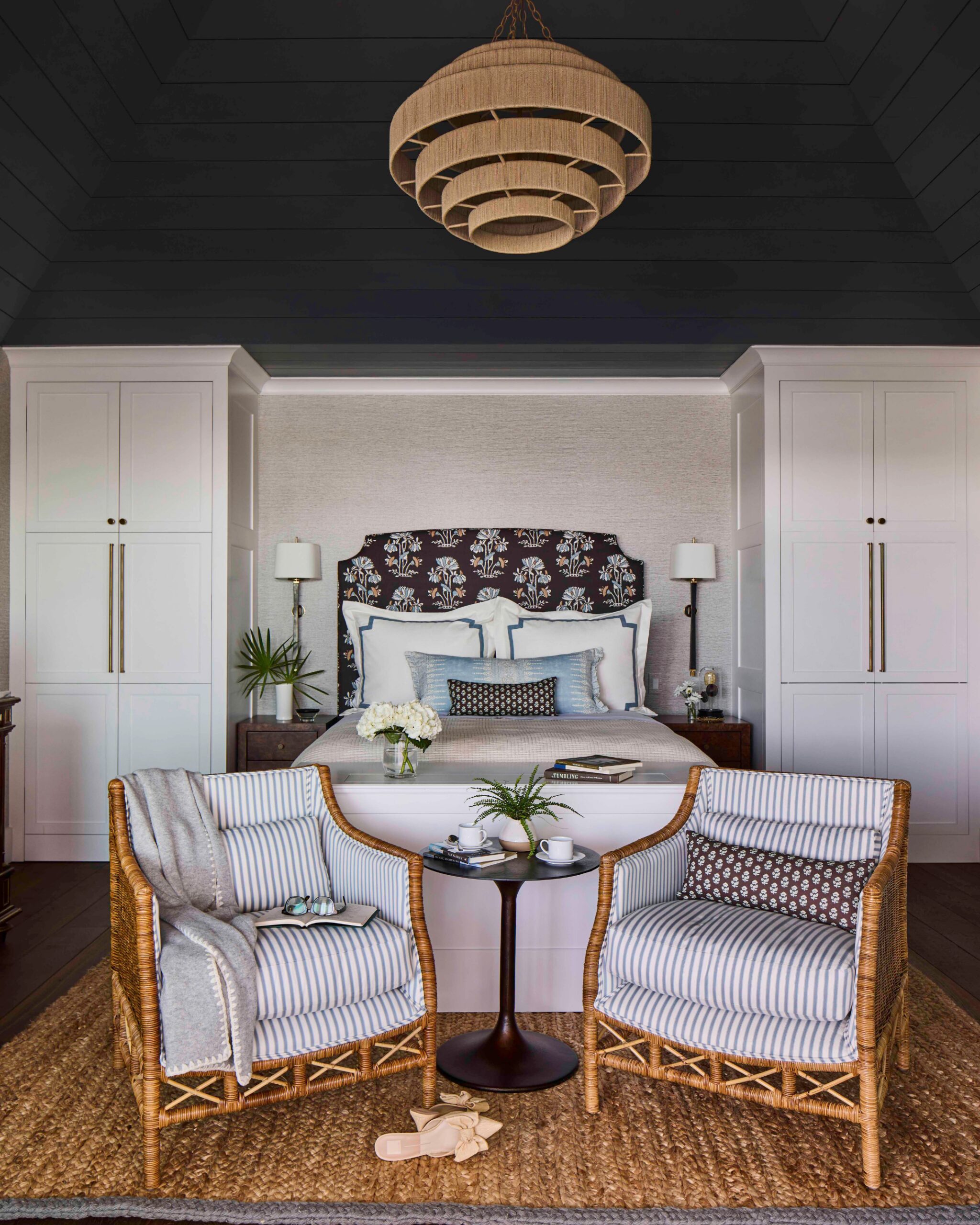 Bedroom with a dark vaulted ceiling, woven pendant, and rattan armchairs in the 2025 Southern Living Showcase Home in Habersham, SC, built by Allen Patterson Builders