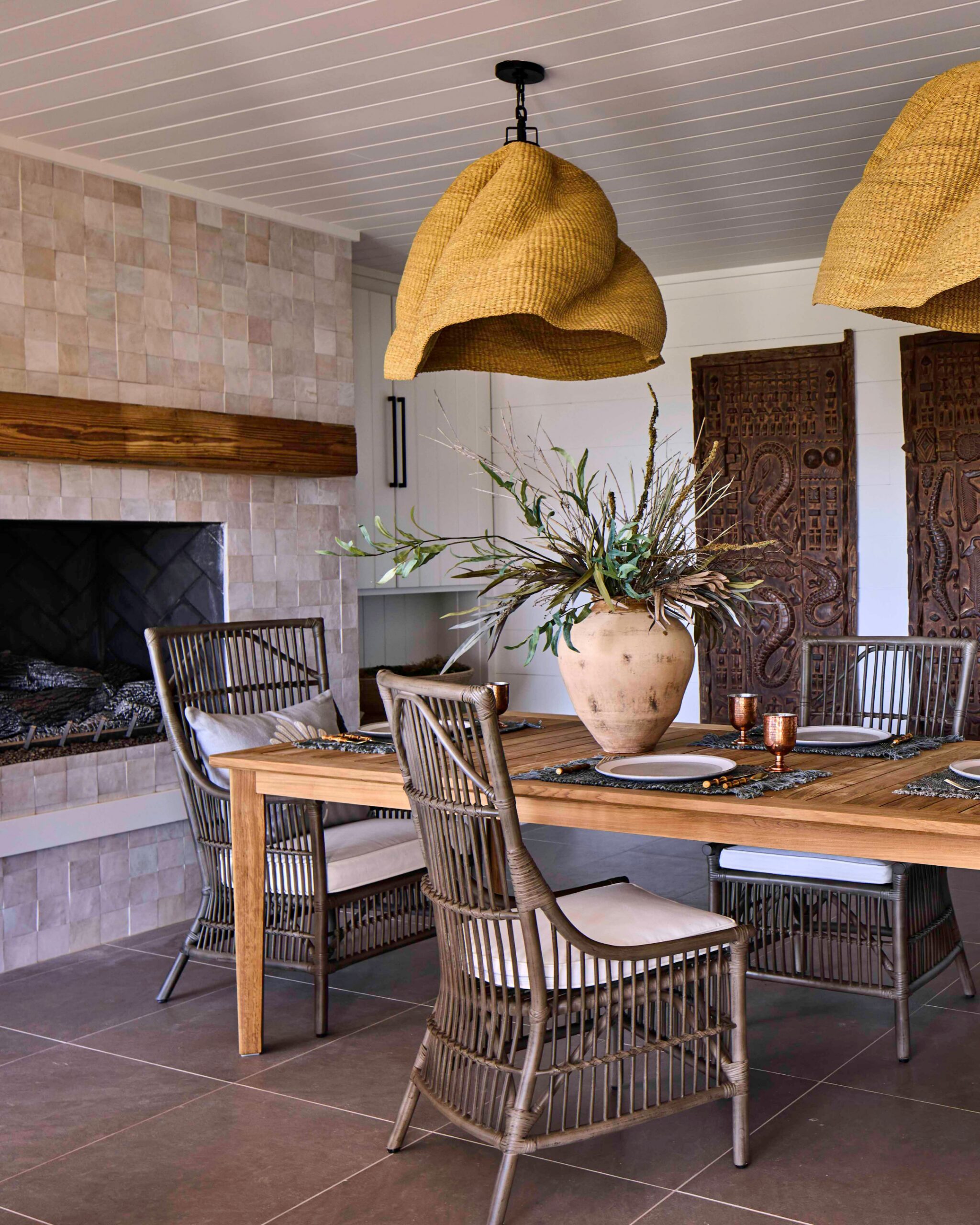 Covered porch dining area with a fireplace, rattan chairs, and woven pendants in the 2025 Southern Living Showcase Home in Habersham, SC, built by Allen Patterson Builders