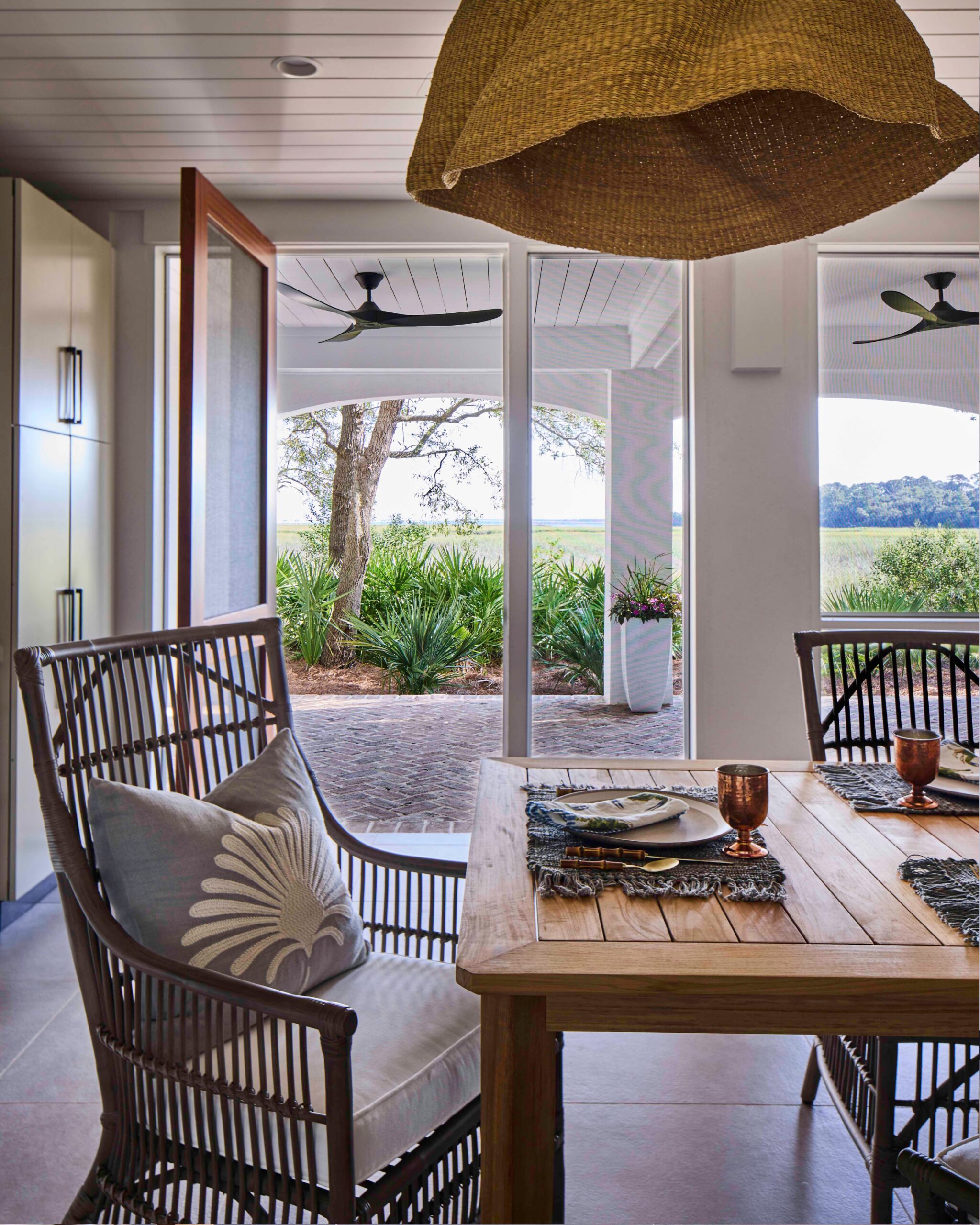 Screened porch with rattan dining furniture and marsh views in the 2025 Southern Living Showcase Home in Habersham, SC, built by Allen Patterson Builders