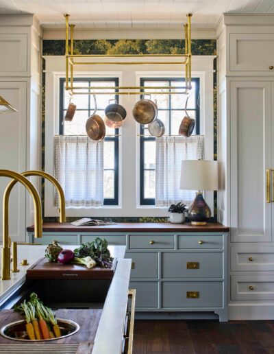Custom kitchen detail in the Habersham Showcase Home with copper pots hung over a window, brass faucet, and pale blue cabinetry, Habersham, SC