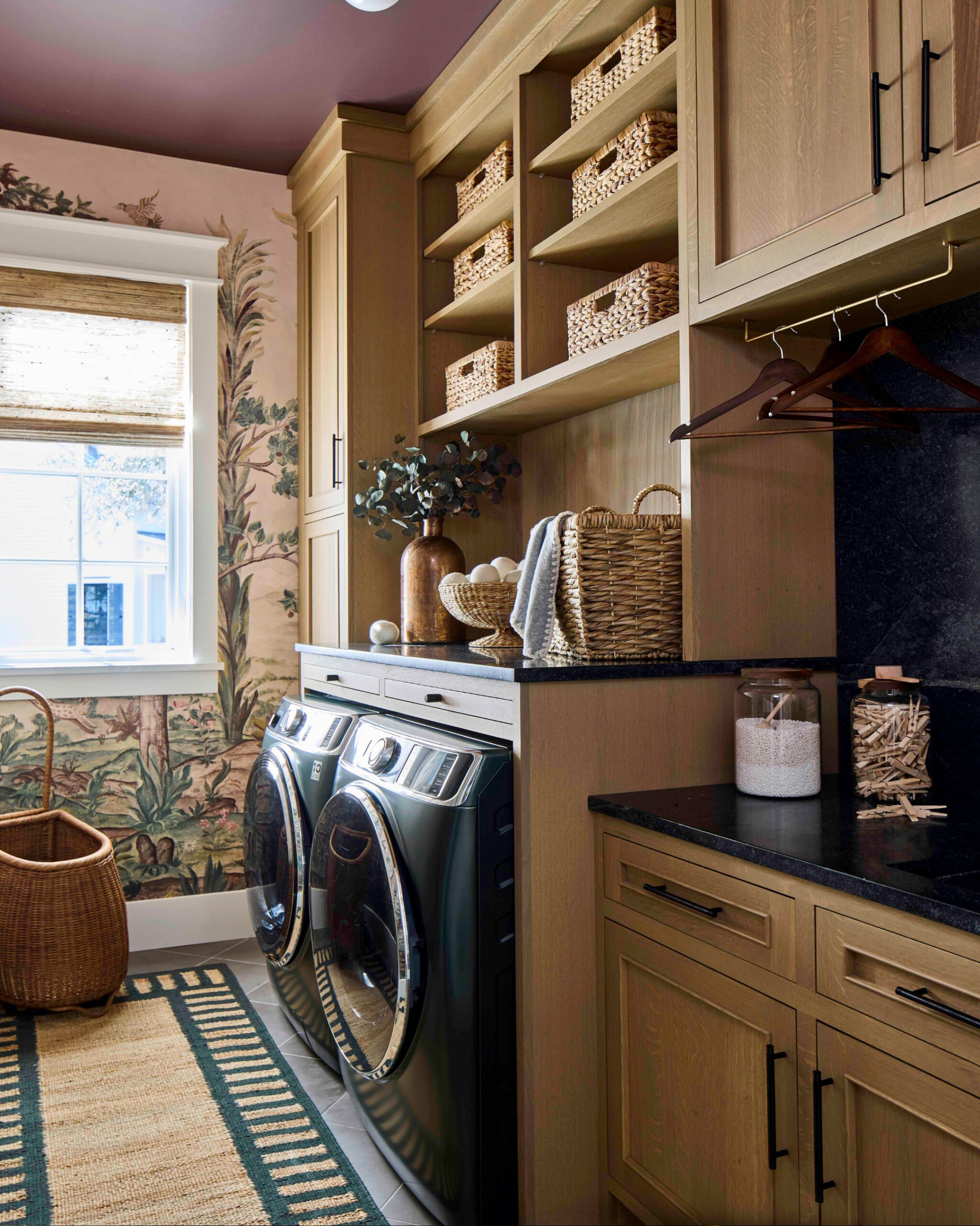 Laundry room with white oak cabinetry, woven baskets, and scenic wallpaper in the 2025 Southern Living Showcase Home in Habersham, SC, built by Allen Patterson Builders