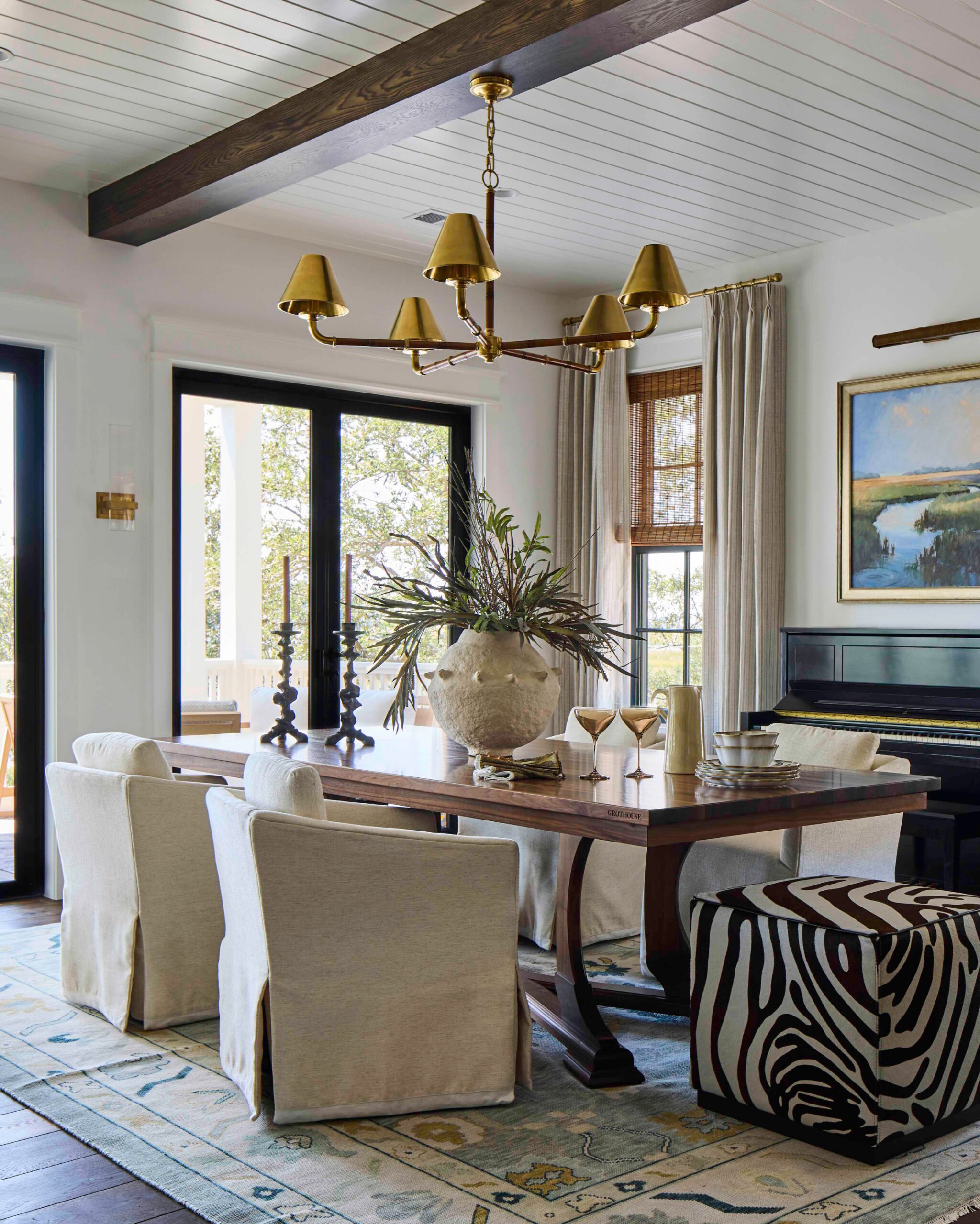 Dining room with a brass chandelier, linen slipcovered chairs, and marsh views in the 2025 Southern Living Showcase Home in Habersham, SC, built by Allen Patterson Builders