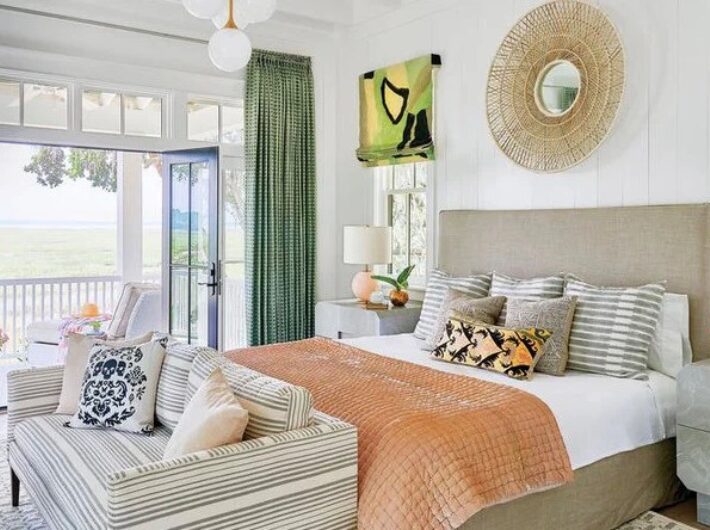 Bedroom in the 2018 Coastal Living Idea House with an upholstered bed, green curtains, and French doors opening to a marsh-view porch.